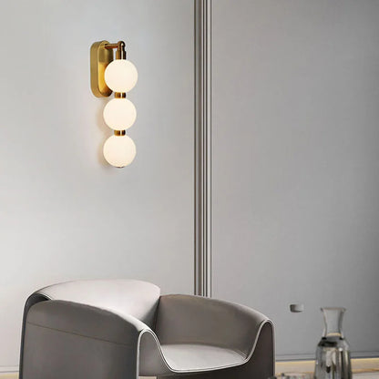Vägglampa med tre akrylkulor och gyllene metallbas